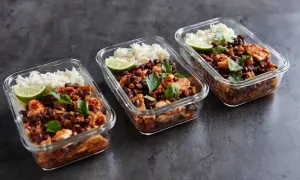 Drei Glasbehälter mit meal prep reis, Hähnchen, schwarzen Bohnen und Limettenspalten, garniert mit Petersilie.