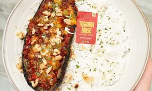 Gefüllte Aubergine mit einer würzigen Tofu-Bolognese-Mischung, garniert mit Walnüssen und Petersilie, serviert mit Reis.