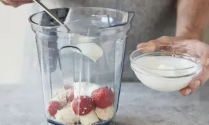 Joghurt wird mit Erdbeeren, Bananen und Haferflocken in einen Mixer gegeben. Ein gesunder Smoothie mit Haferflocken entsteht.