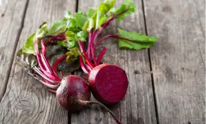 Zwei frische rote Bete, eine davon halbiert, liegen auf rustikalem Holz. Perfekt, um rote Beete roh zu essen und die gesunden Nährstoffe zu genießen.