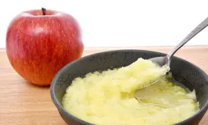 Ein roter Apfel neben einer Schüssel mit Apfelmus, ideal bei Magen-Darm-Beschwerden.