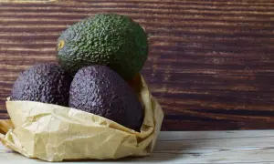 Drei Avocados liegen in einer Papiertüte. Eine grüne Avocado liegt obenauf, zwei dunklere darunter. So kann man Avocados lagern.
