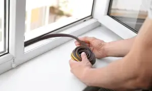 Hände halten eine aufgerollte Fensterdichtung bereit, um sie am Fensterrahmen anzubringen. Fensterdichtung erneuern für mehr Gemütlichkeit.