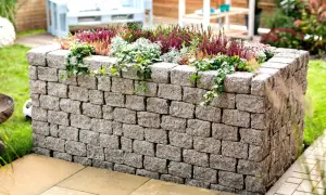 Ein bepflanztes Hochbeet mit stabilen hochbeet mauern aus Betonsteinen, umgeben von grünem Rasen und einer Terrasse.