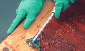 Grüne Handschuhe entfernen mit einem Werkzeug rote Farbe, um das Holz abbeizen.