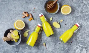 Zutaten für ein Ingwer Shot Rezept: frischer Ingwer, Zitrone, Honig und drei Flaschen des gelben Shots.