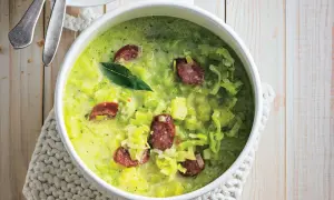 Herzhafter porree eintopf mit würziger Wurst und einem Lorbeerblatt, serviert in einer weißen Schüssel auf einem Holztisch.