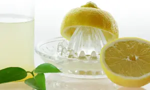 Frisch gepresster Zitronensaft in einem Glas, bereit zur Lagerung. Eine halbe Zitrone liegt auf einer Zitruspresse.