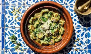 Spinat Ricotta Gnocchi, garniert mit Parmesan und Zitrone, serviert in einer Terrakotta-Schale auf blau-weißen Fliesen.