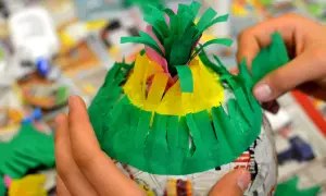 Hände basteln eine bunte Piñata. Mit grünem Krepppapier wird die Form verziert, um eine Piñata selber machen zu können.