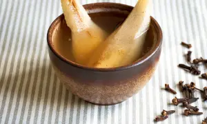 Zwei Birnenspalten in einer Schale mit Flüssigkeit, ein zuckerfreies Birnenkompott. Gewürznelken liegen daneben.