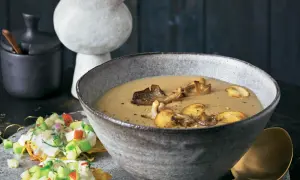 Herzhafte pilz suppe in einer rustikalen Schüssel, garniert mit gebratenen Pilzen. Daneben ein kleiner Salat mit Apfel und Kräutern.