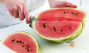 So schneidest du eine Wassermelone richtig: Ein Messer teilt die saftige Frucht in zwei Hälften, eine davon liegt bereits als Stück daneben.