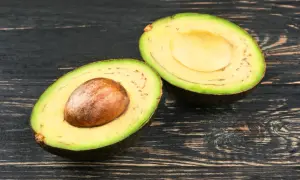 Eine aufgeschnittene Avocado mit Kern und einigen kleinen schwarzen Punkten im Fruchtfleisch liegt auf dunklem Holz.