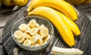 Bananen auf einem Holzteller, eine Schüssel mit Bananenscheiben und eine geschälte Banane. Interessiert, wie viel Zucker hat eine Banane?