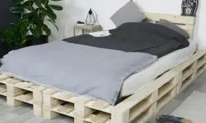 Ein rustikales Bett, das man einfach selber bauen kann, aus Europaletten. Mit grauer Decke und Kissen.