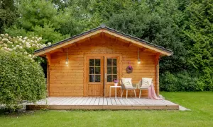 Ein gemütliches Gartenhaus, das man gut selber bauen kann, mit Veranda, zwei Stühlen und einer Tür.