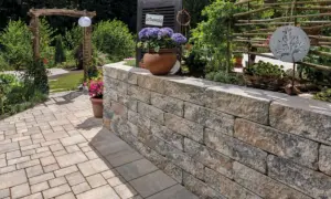 Eine stabile gartenmauer bauen aus Natursteinblöcken, die den Gartenbereich stilvoll abgrenzt und mit Blumen und Pflanzen dekoriert ist.