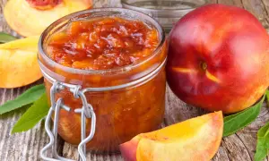 Glas mit leuchtend orangefarbener Nektarinen Marmelade, daneben frische Nektarinen und Fruchtstücke auf rustikalem Holz.