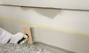Mit einem Pinsel wird der Sockel verputzt. Klebeband schützt die Wand.