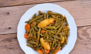Ein Teller mit einem köstlichen Fasolakia Rezept, das grüne Bohnen, Kartoffeln und Karotten in einer würzigen Sauce zeigt.
