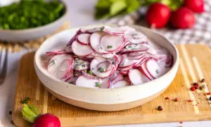 Frischer radieschensalat mit joghurt und schnittlauch, garniert mit pfefferkörnern.