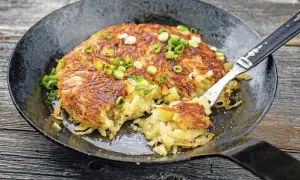Herzhaft gebratene Kartoffelpuffer, perfekt für Meal Prep Kartoffeln, garniert mit Frühlingszwiebeln in einer Gusseisenpfanne.