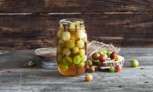 Ein Glas mit stachelbeeren einkochen, daneben liegen einige frische Beeren auf Holzscheiben.