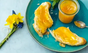 Quittenrezepte Marmelade auf Brot, daneben ein Glas mit der leuchtend gelben Marmelade und ein Löffel. Ein Frühlingsstrauß mit Narzissen und Traubenhyazinthen.
