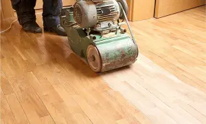 Ein Handwerker bearbeitet mit einer Schleifmaschine einen Holzboden. Das Parkett abschleifen erweckt den alten Boden zu neuem Glanz.