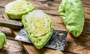 Frischer Spitzkohl, halbiert und auf einem Holzbrett mit einem Hackmesser. Perfekt, um Spitzkohl roh zu essen für einen knackigen Salat.