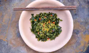 So einfach lassen sich getrocknete Algen zubereiten: Ein Teller mit mariniertem Seetang, bestreut mit Sesam und Chili. Stäbchen liegen bereit.