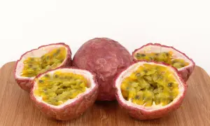 Ein ganzes und vier halbierte Passionsfrüchte liegen auf einem Holzbrett. Die Fruchtkerne sind saftig und gelb. Perfekt zum Passionsfrucht essen!