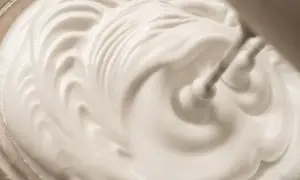 Sahne steif schlagen ohne Sahnesteif: Ein Handmixer formt cremige Wellen in der weißen Masse.