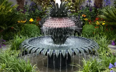 Ein kunstvoller Gartenbrunnen im Ananas-Design, der zum **gartenbrunnen selber bauen** inspiriert. Umgeben von üppiger Vegetation und bunten Blumen.