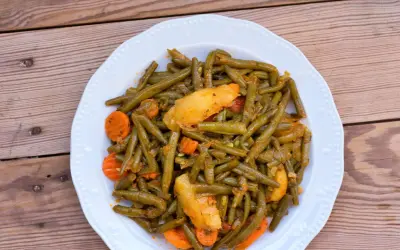 Ein Teller mit einem köstlichen Fasolakia Rezept, das grüne Bohnen, Kartoffeln und Karotten in einer würzigen Sauce zeigt.