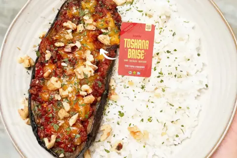 Gefüllte Aubergine mit einer würzigen Tofu-Bolognese-Mischung, garniert mit Walnüssen und Petersilie, serviert mit Reis.