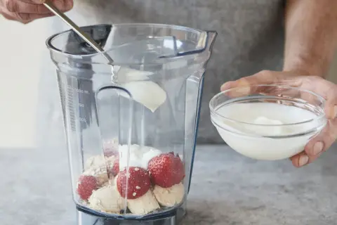 Joghurt wird mit Erdbeeren, Bananen und Haferflocken in einen Mixer gegeben. Ein gesunder Smoothie mit Haferflocken entsteht.