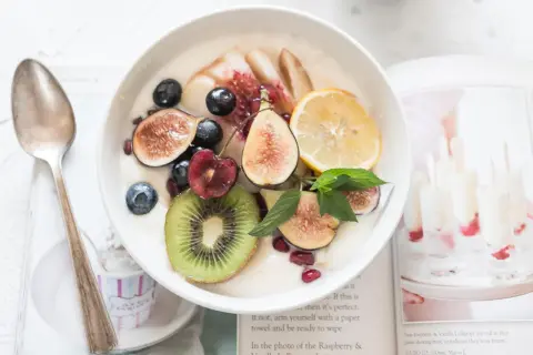 Schüssel mit Kokosjoghurt, garniert mit Feigen, Beeren, Kiwi und Zitrone. Ein gesundes Frühstück, das Lust auf mehr macht.