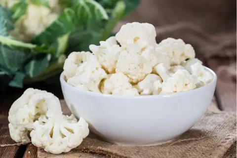 Frischer blumenkohl roh essen ist gesund und lecker. Hier sind Röschen in einer Schüssel und daneben auf einem Holzbrett.