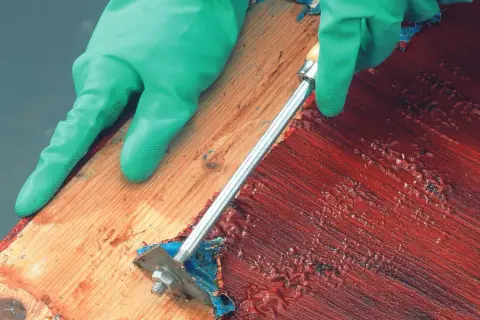 Grüne Handschuhe entfernen mit einem Werkzeug rote Farbe, um das Holz abbeizen.