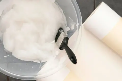 Schüssel mit selbstgemachtem Kleister und Pinsel, dane liegen Tapetenrollen bereit.