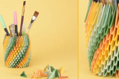 Bunter Stiftehalter aus Origami-Modulen, inspiriert von Papier Ideen. Daneben liegen bunte Papierbögen und kleine Origami-Figuren.