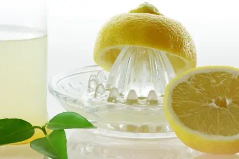 Frisch gepresster Zitronensaft in einem Glas, bereit zur Lagerung. Eine halbe Zitrone liegt auf einer Zitruspresse.