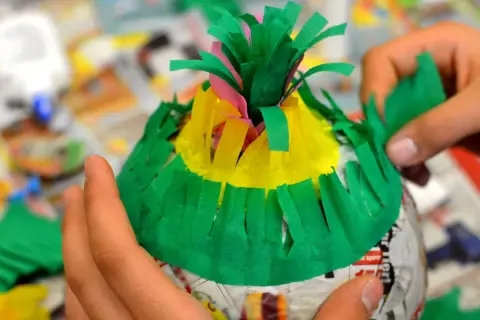 Hände basteln eine bunte Piñata. Mit grünem Krepppapier wird die Form verziert, um eine Piñata selber machen zu können.