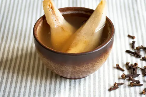 Zwei Birnenspalten in einer Schale mit Flüssigkeit, ein zuckerfreies Birnenkompott. Gewürznelken liegen daneben.