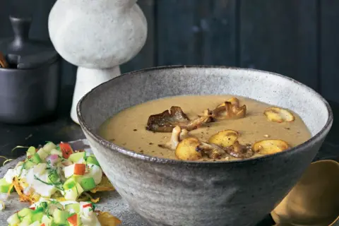 Herzhafte pilz suppe in einer rustikalen Schüssel, garniert mit gebratenen Pilzen. Daneben ein kleiner Salat mit Apfel und Kräutern.