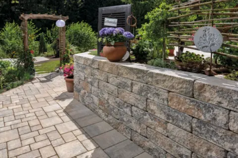 Eine stabile gartenmauer bauen aus Natursteinblöcken, die den Gartenbereich stilvoll abgrenzt und mit Blumen und Pflanzen dekoriert ist.