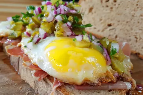 Ein **strammer Max vegetarisch** mit Spiegelei, Schinken, Gewürzgurken und Zwiebeln auf rustikalem Brot.
