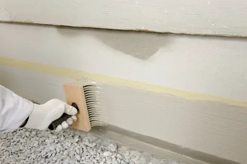 Mit einem Pinsel wird der Sockel verputzt. Klebeband schützt die Wand.